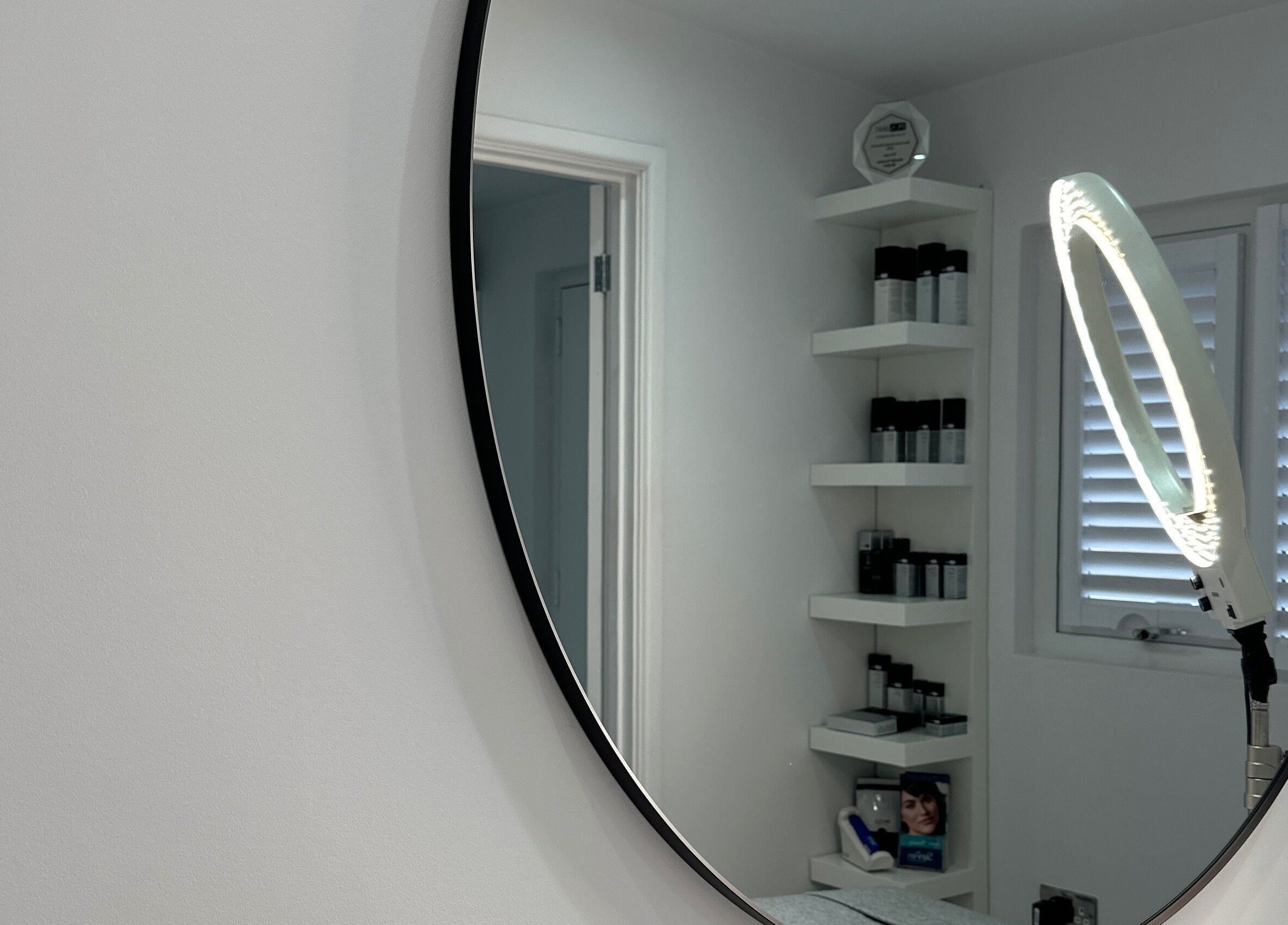 Elegant oval mirror at Sknject, Rotherham, England, GB, reflecting minimalist shelves and beauty equipment.