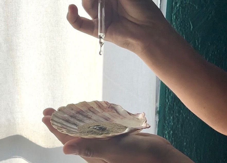 Manos sosteniendo concha en East Therapy, Barcelona, Catalunya, ES, mostrando esencia goteando.