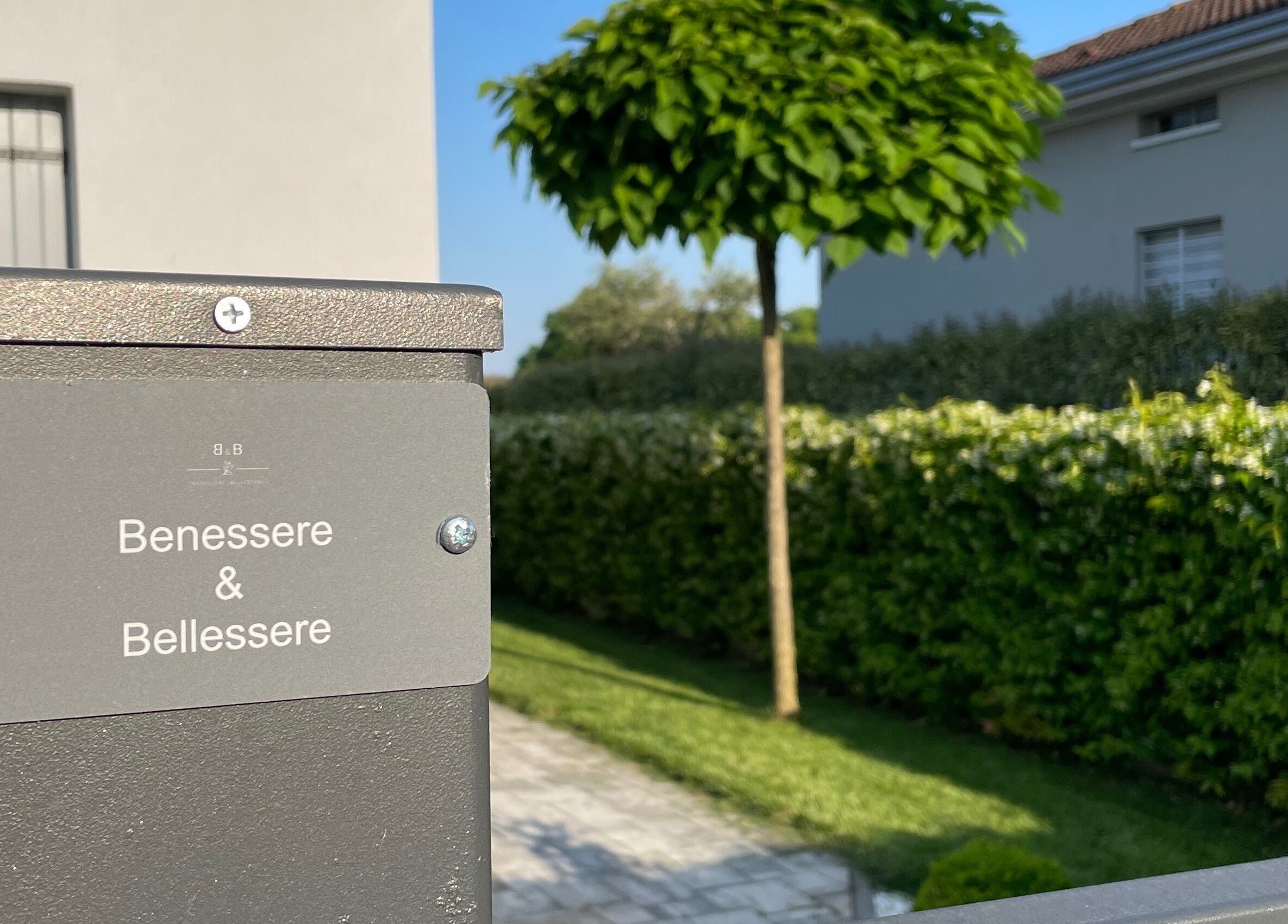 Ingresso di Benessere & Bellessere a Vigasio, Veneto, IT, con vegetazione lussureggiante.