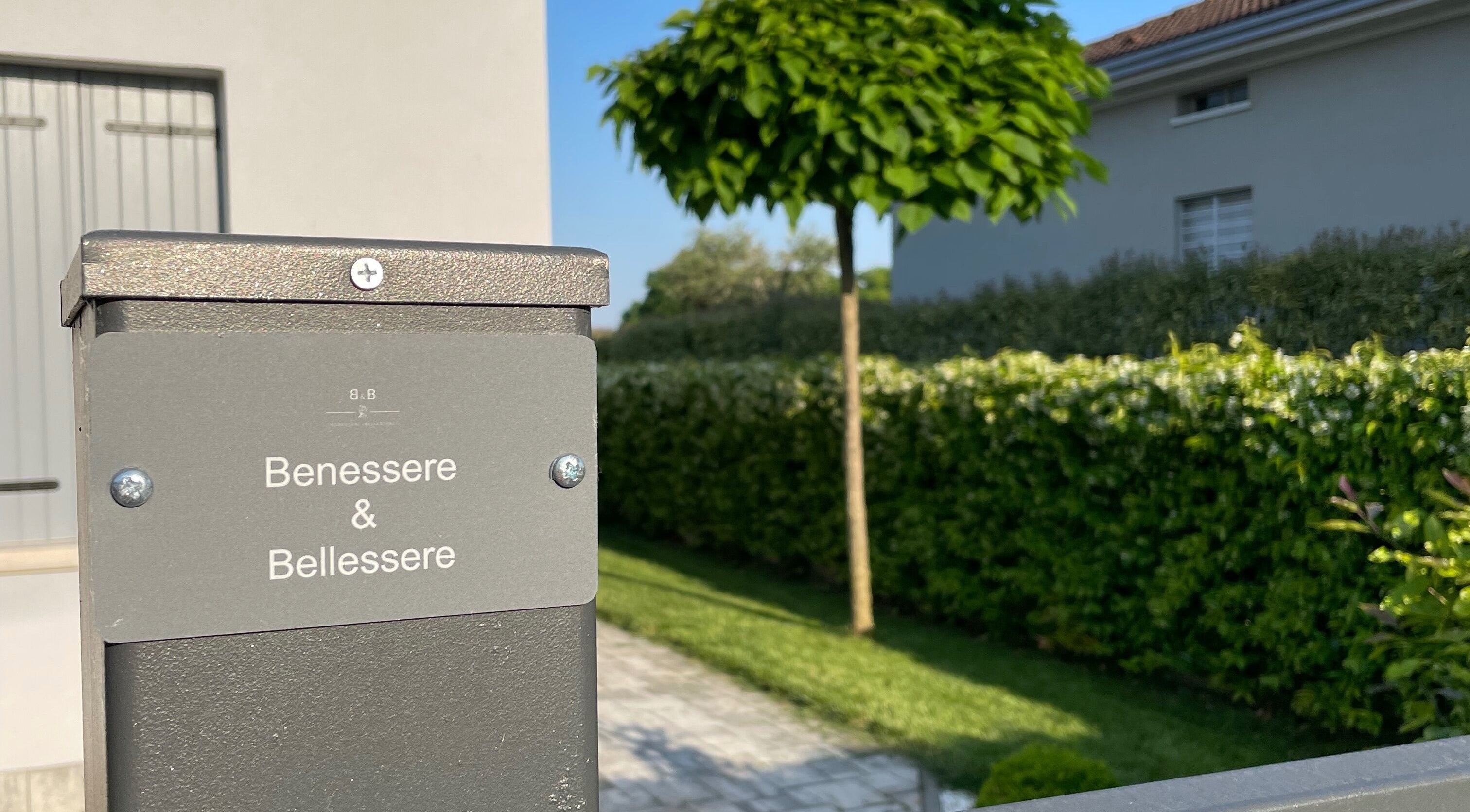 Ingresso di Benessere & Bellessere a Vigasio, Veneto, IT, con vegetazione lussureggiante.