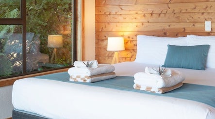 Cozy spa room at Kimi Ora Day Spa in Kaiteriteri, Tasman, NZ featuring a bed with fresh towels and wood-panel walls.