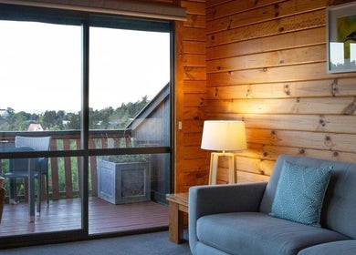Cozy interior at Kimi Ora Day Spa in Kaiteriteri, Tasman, NZ with sofa, lamp, and balcony view.