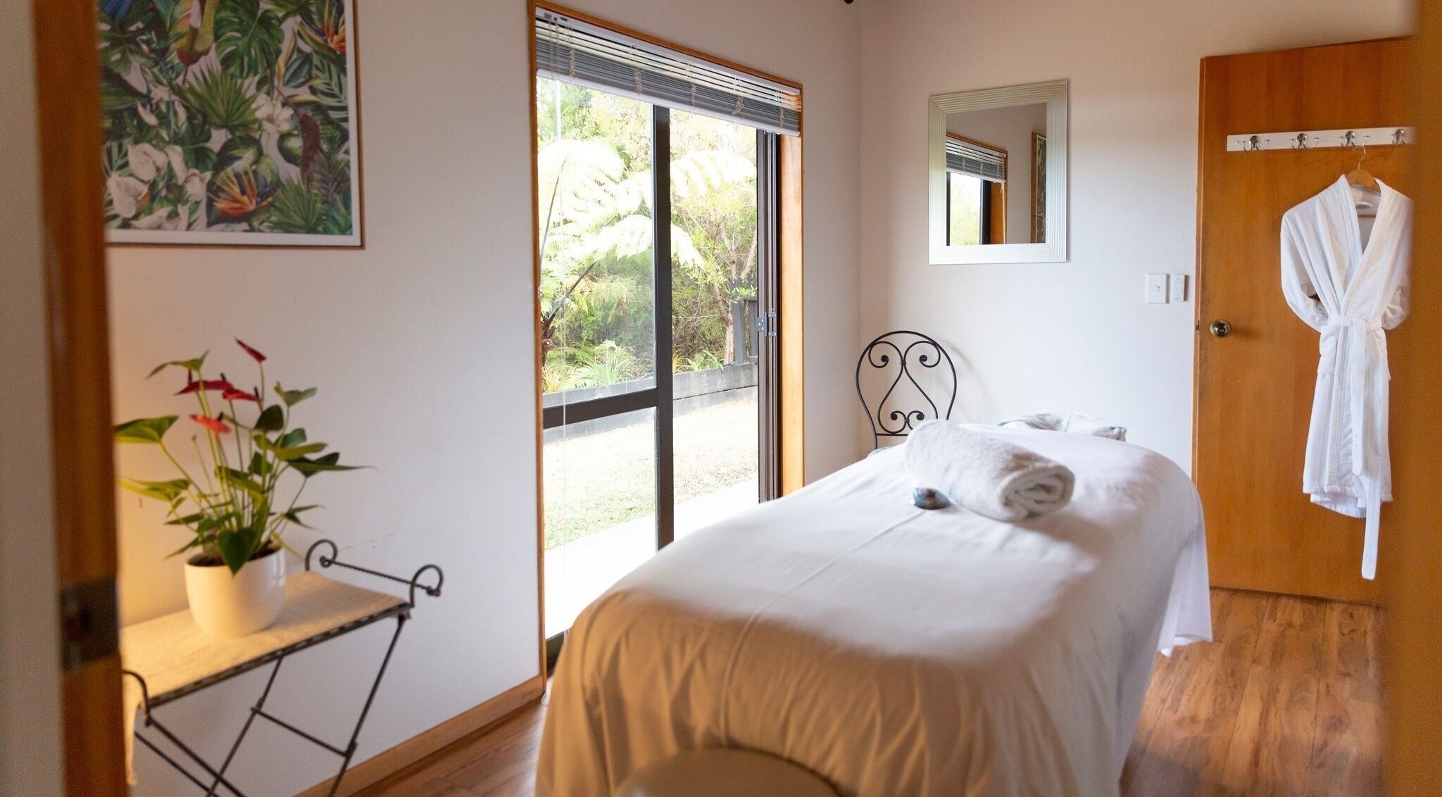 Tranquil spa room at Kimi Ora Day Spa in Kaiteriteri, Tasman, NZ, featuring massage bed and nature views.