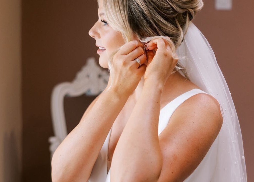 Bride adjusting earrings at G L O Y À, Rochester, England, GB. Serene ambiance for weddings.