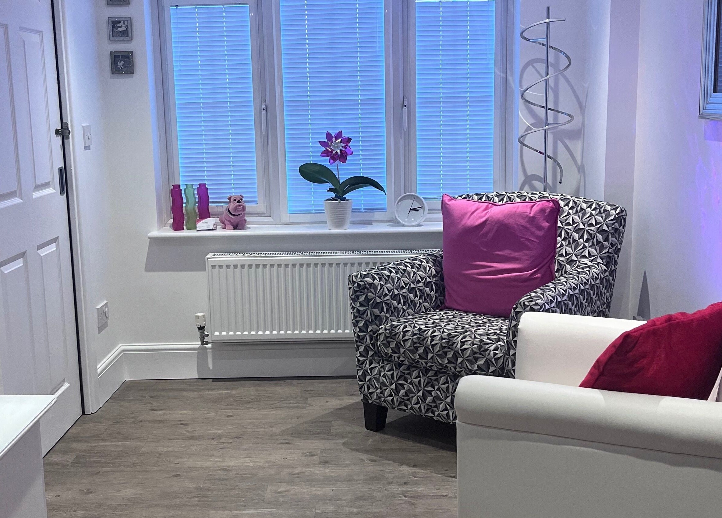 Cozy lounge area with patterned armchair and pink accents at BodyLogic, Higham Ferrers, GB.