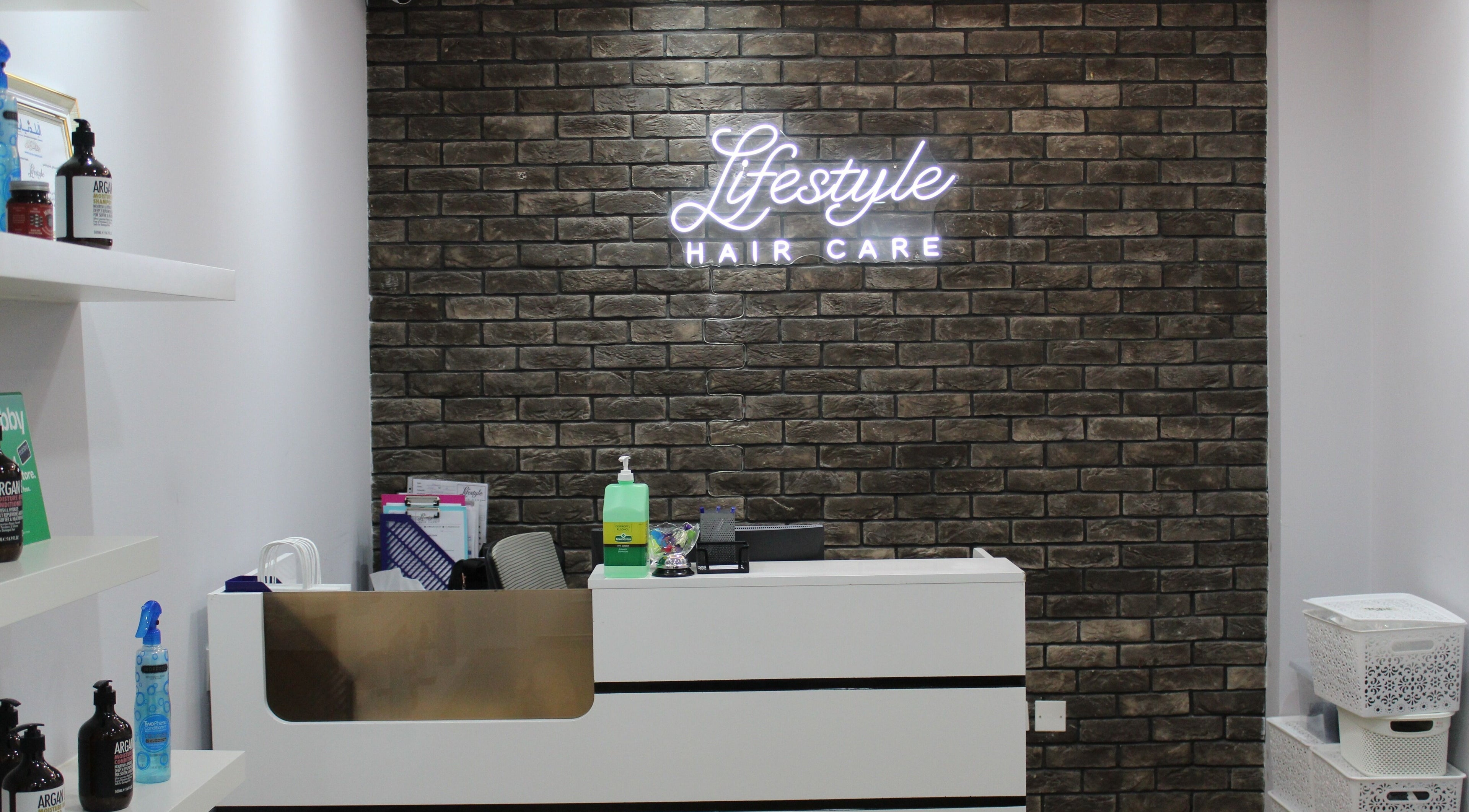 Reception desk at Lifestyle Hair Care, دبي, دبي, AE, with modern brick wall and product shelf.