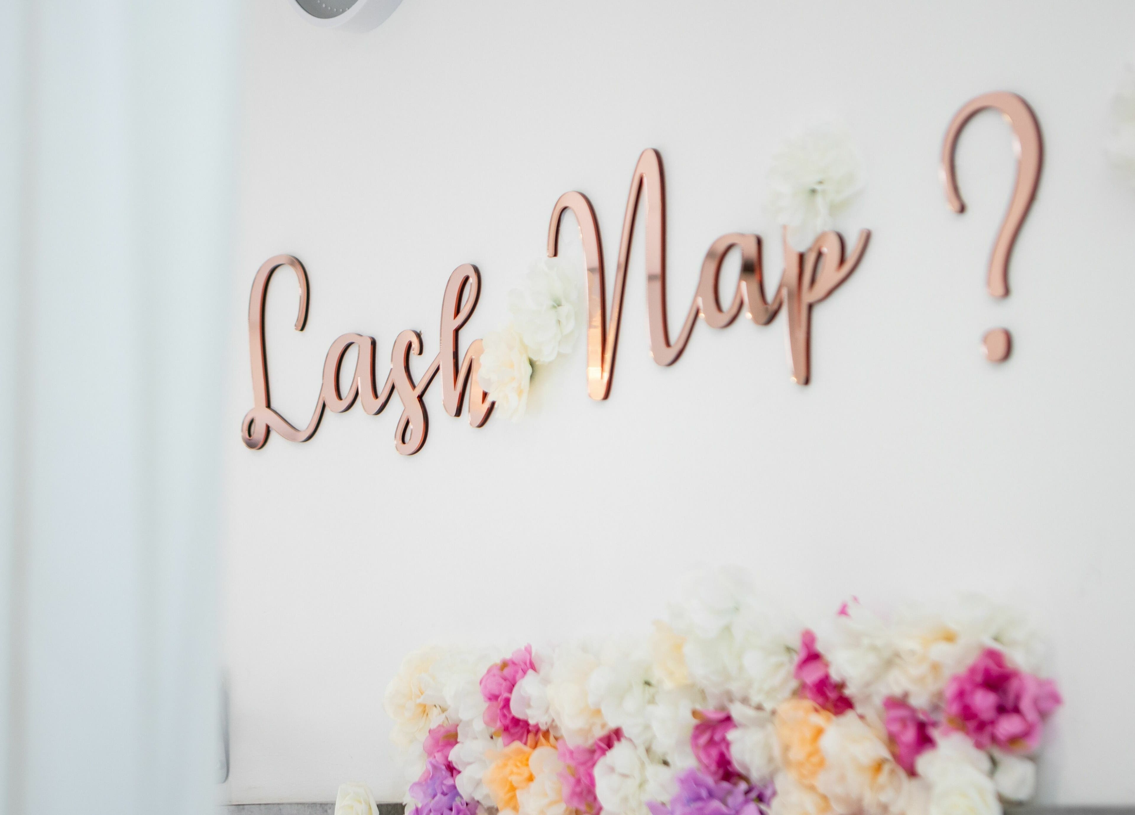Floral wall with 'Lash Nap?' sign at 10:15 Aesthetics, London, England, GB offering relaxing beauty services.