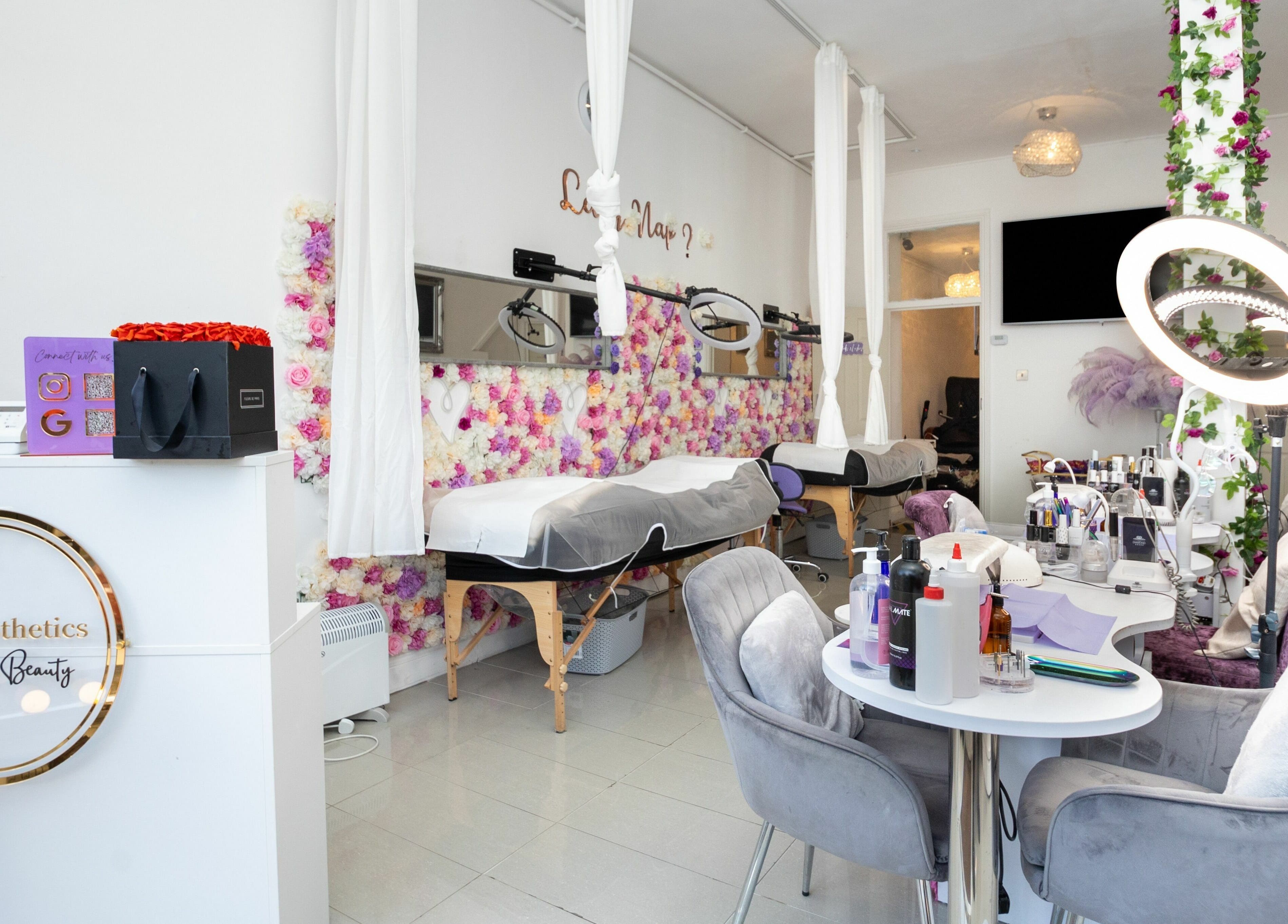 Bright interior of 10:15 Aesthetics, London, England, GB, featuring flower wall, salon beds, and modern decor.