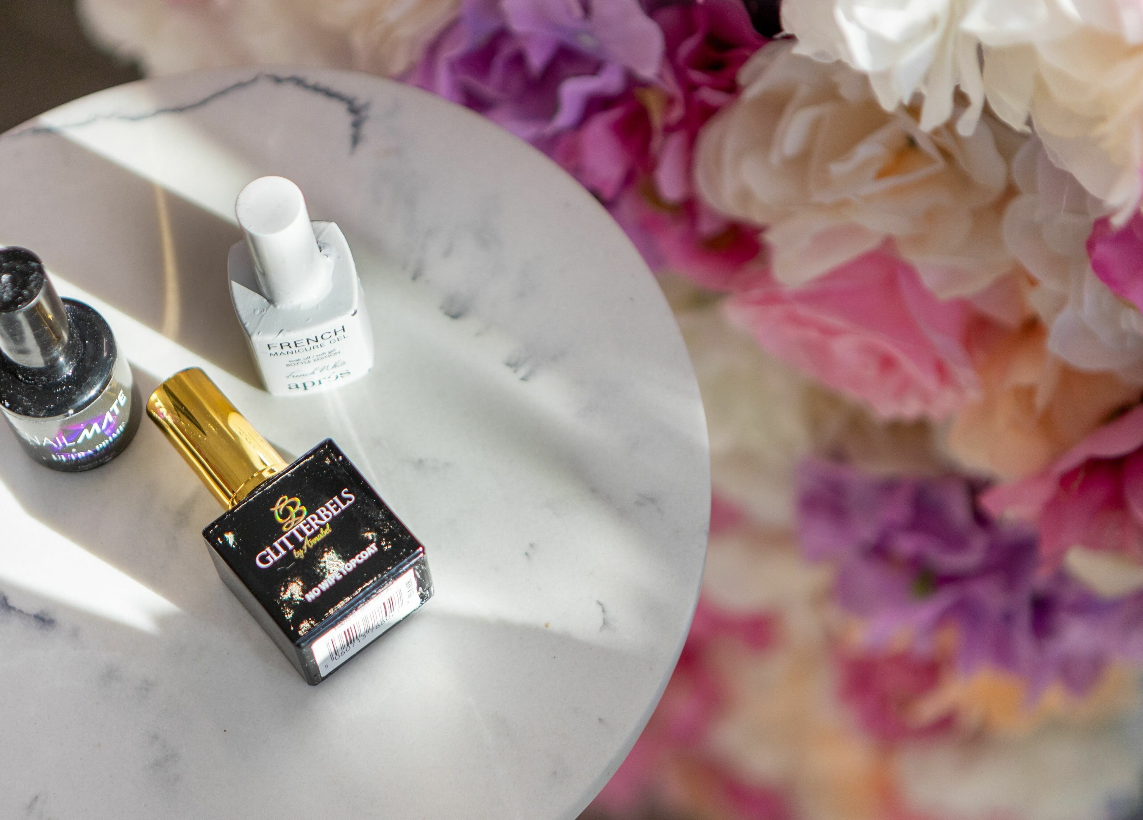 Nail products on marble at 10:15 Aesthetics, London, England, GB, surrounded by vibrant flowers.