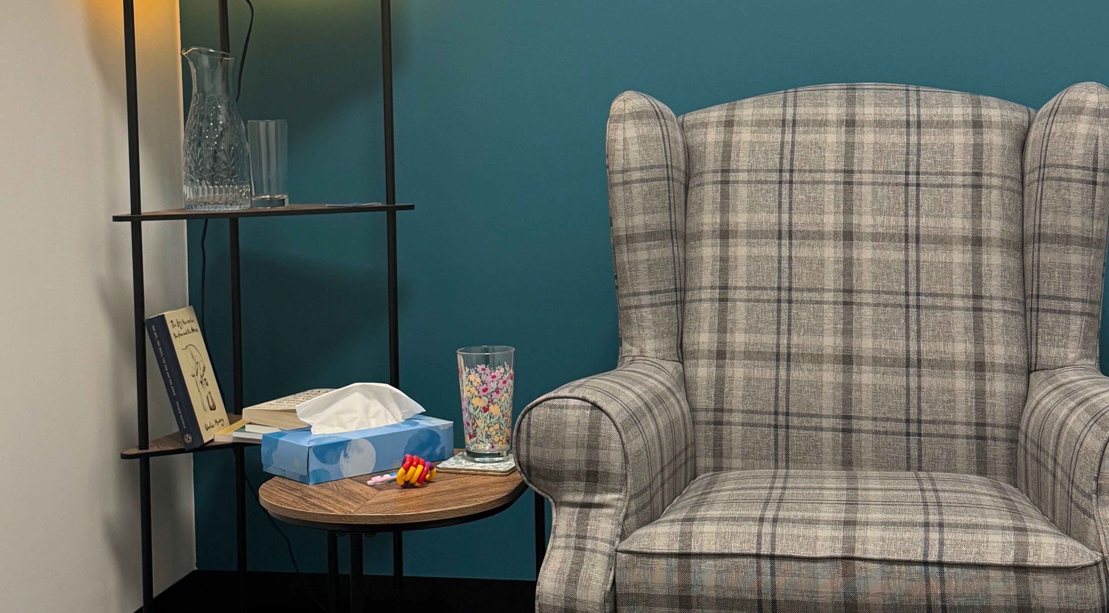 Comfortable plaid chair in Emily Nicholls Counselling, Stoke-on-Trent, England, GB with shelf and decor.