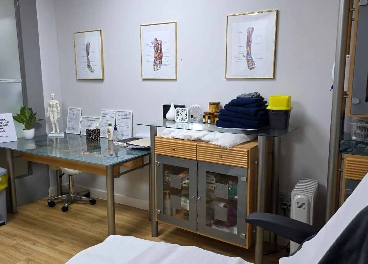 Treatment room at All Being Well Health & Acupuncture in Ilkeston, England. Features charts and a massage table.