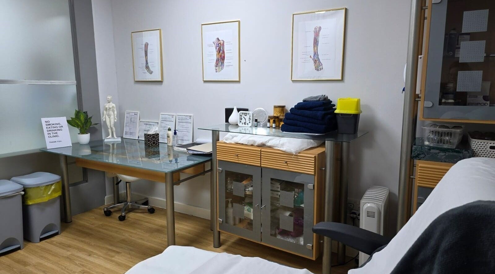 Treatment room at All Being Well Health & Acupuncture in Ilkeston, England. Features charts and a massage table.