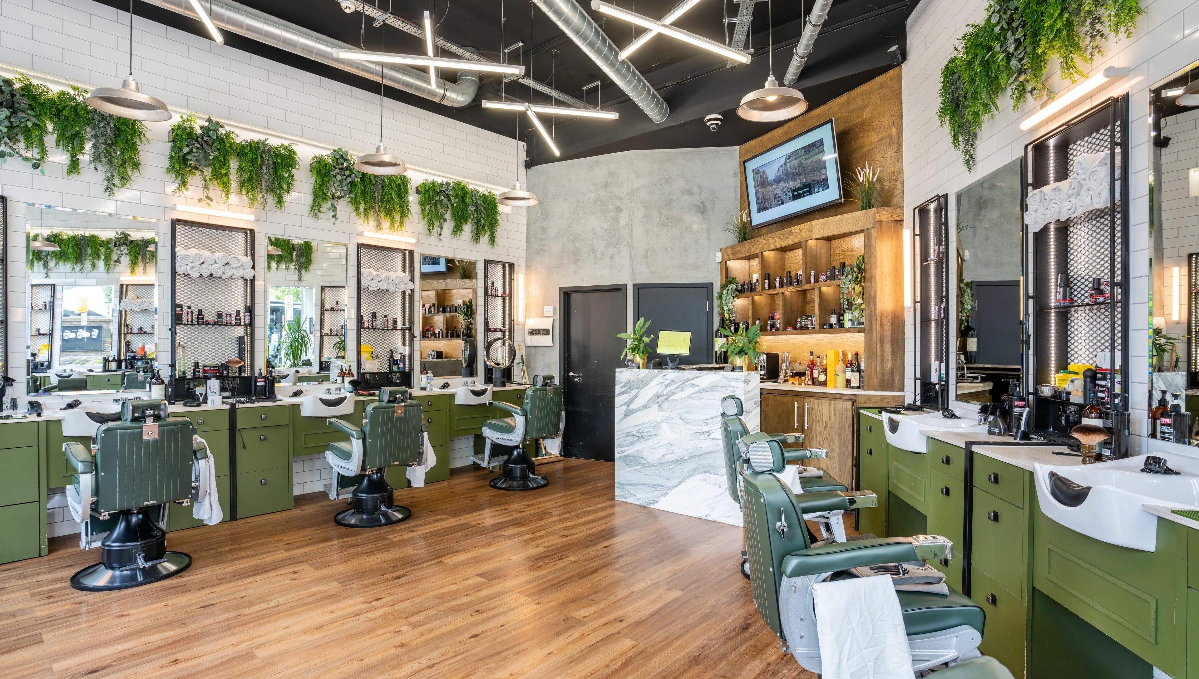Stylish salon interior at The Axe Club in Camden, London, England, GB with green chairs and lush greenery.