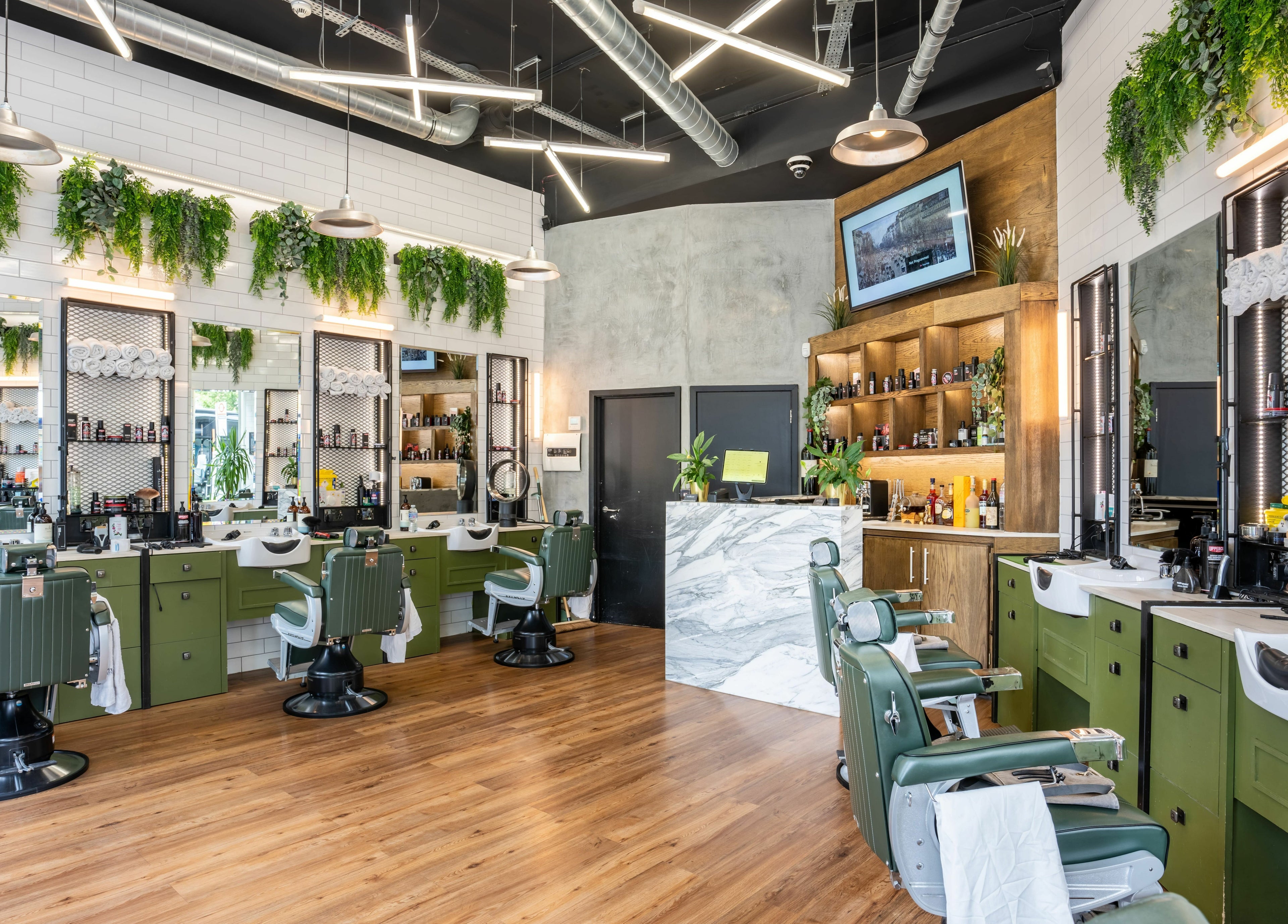 Stylish salon interior at The Axe Club in Camden, London, England, GB with green chairs and lush greenery.