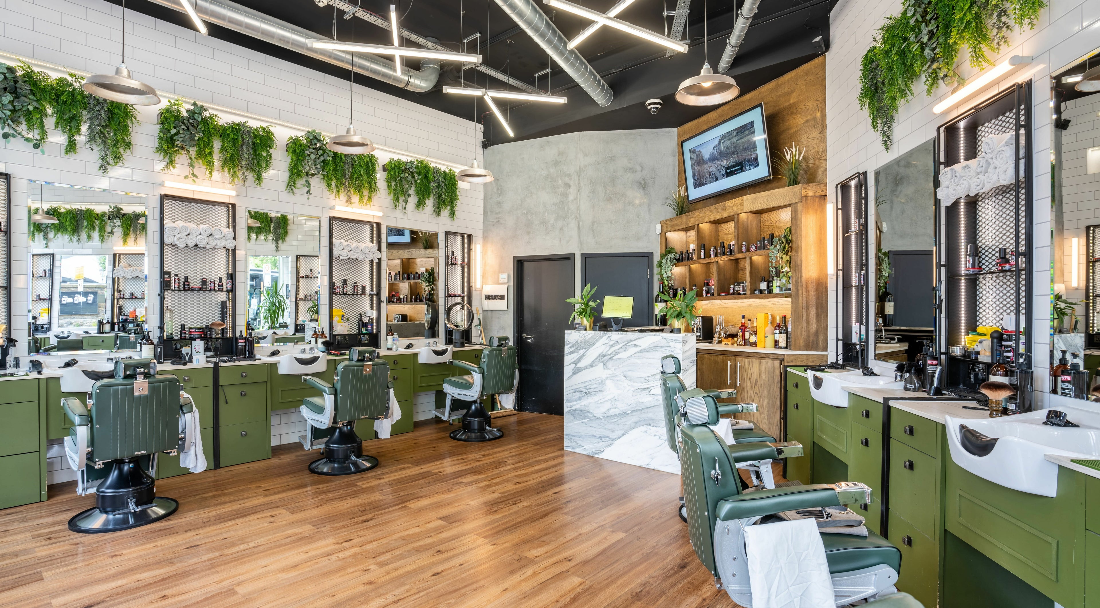 Stylish salon interior at The Axe Club in Camden, London, England, GB with green chairs and lush greenery.