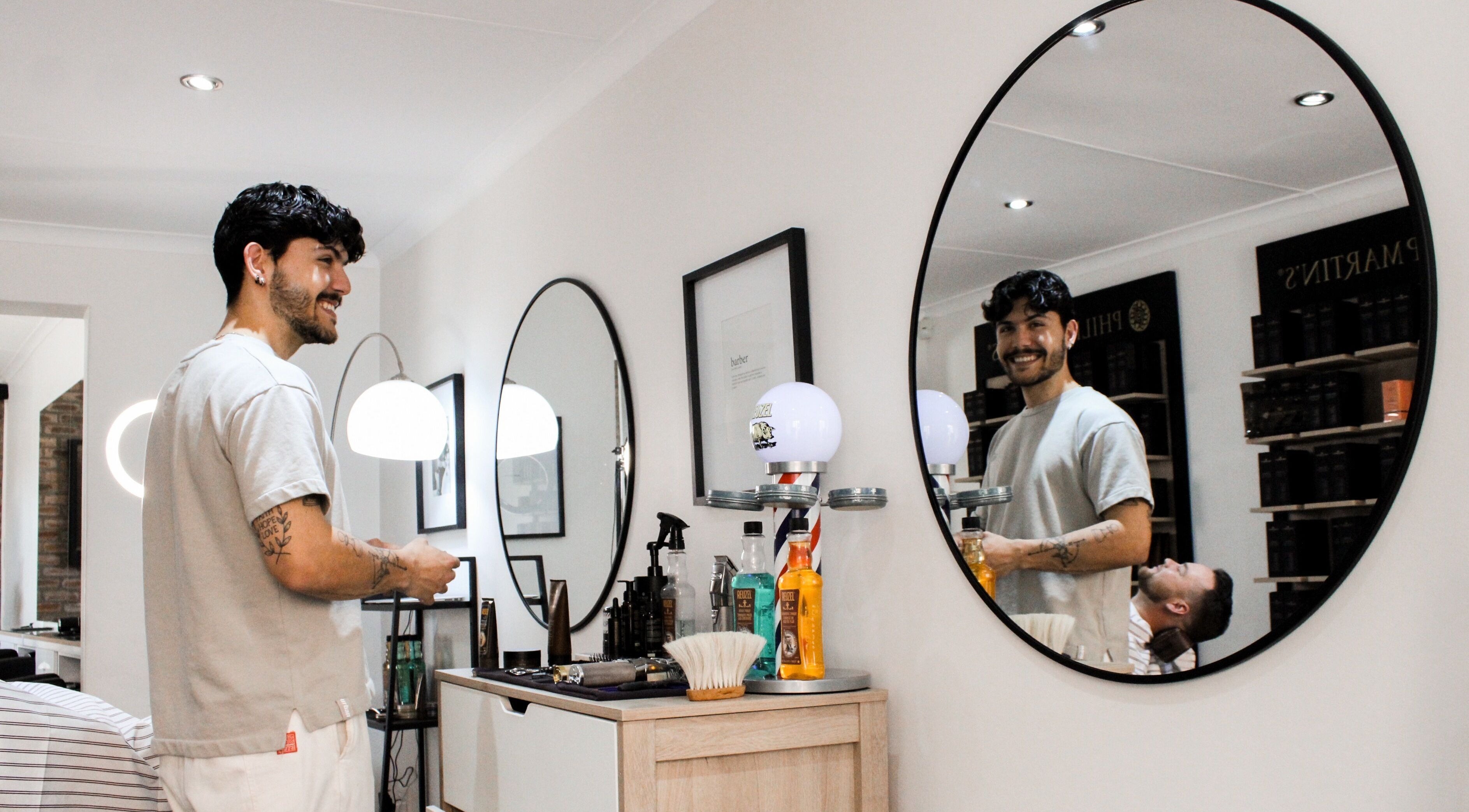 Barber smiling at The Barber in Bloemfontein, Free State, ZA, with a mirror reflection.