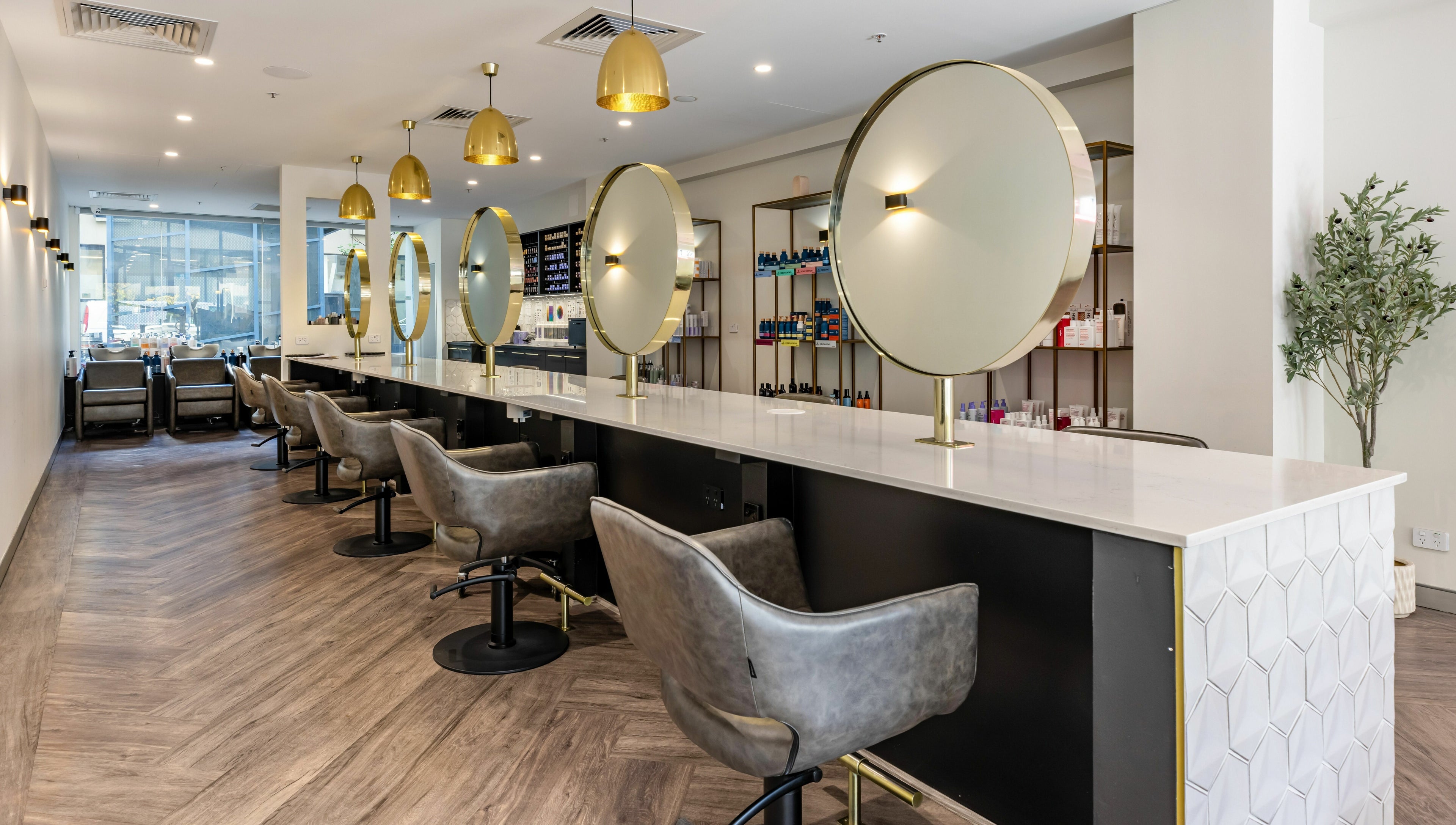 Chic interior of Mooi Hair CBR in Canberra, AU features sleek chairs and mirrors under golden lighting.