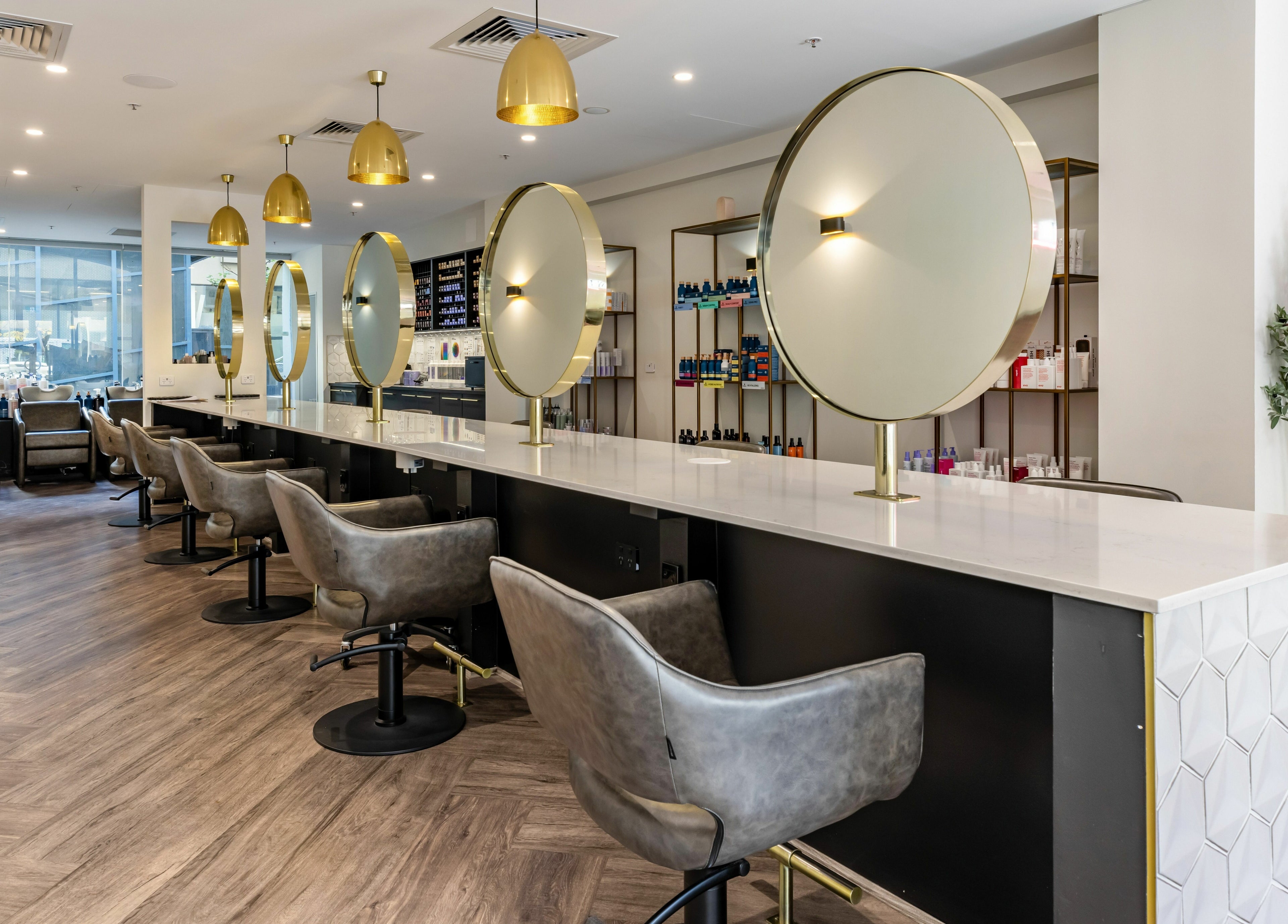 Chic interior of Mooi Hair CBR in Canberra, AU features sleek chairs and mirrors under golden lighting.