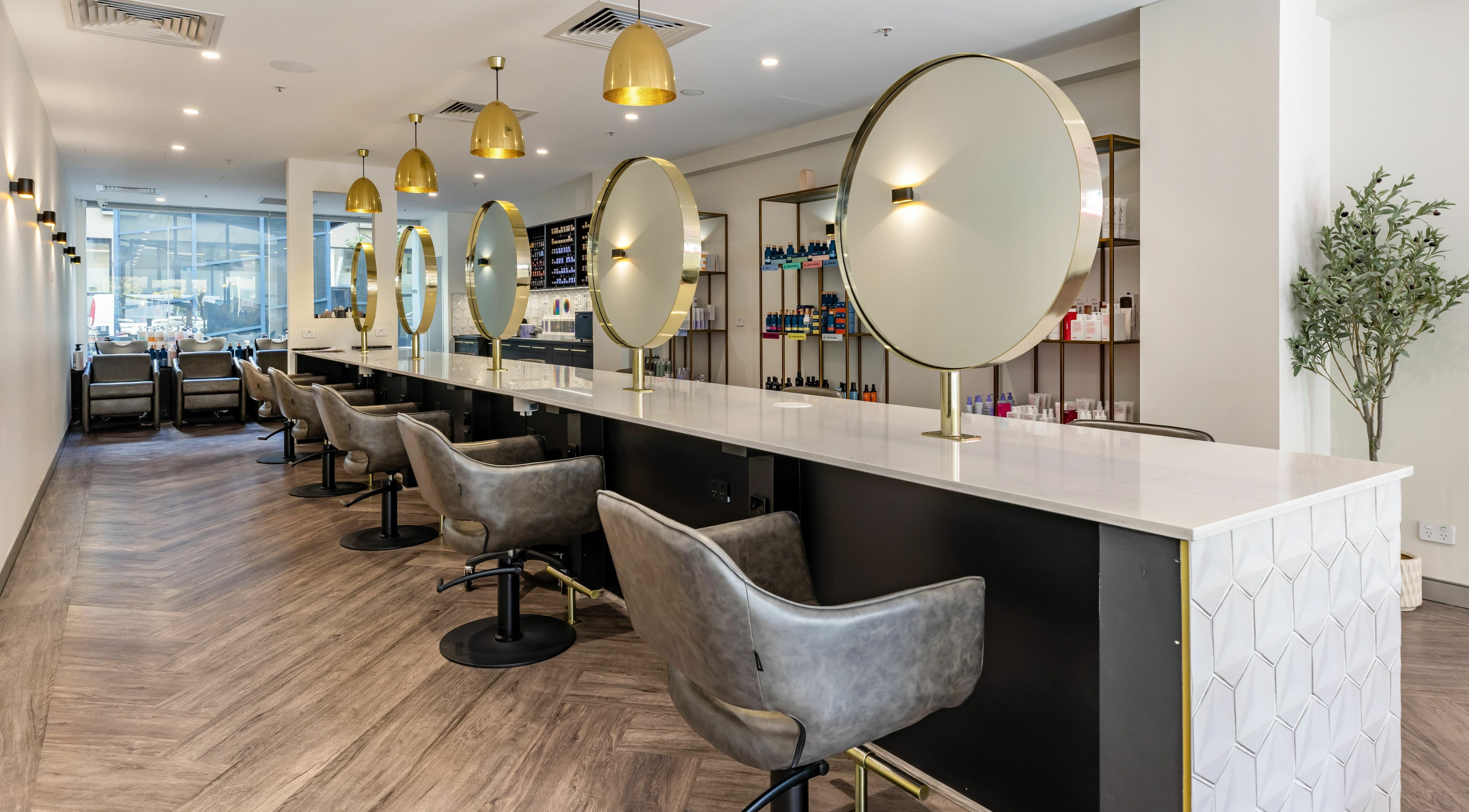 Chic interior of Mooi Hair CBR in Canberra, AU features sleek chairs and mirrors under golden lighting.