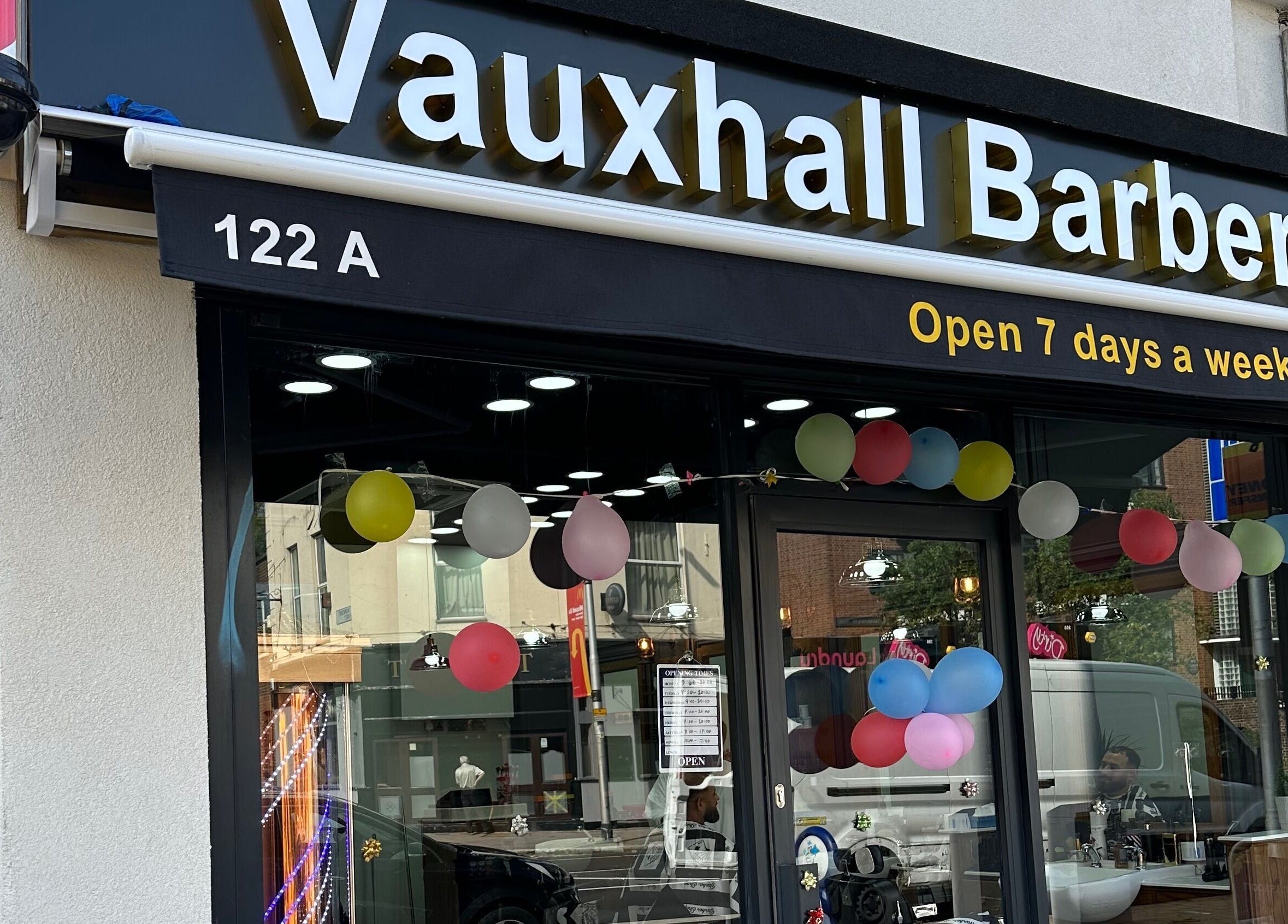 Vauxhall Barbers storefront with balloons in London, England, GB. Open 7 days a week. Welcoming exterior view.