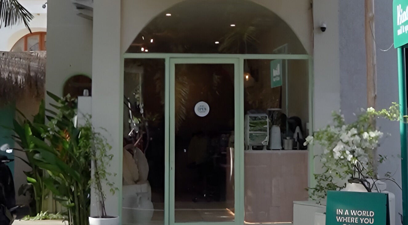 Entrance of Kind - Nails & Spa in Bali, Bali, ID, featuring lush plants and inviting glass doors.