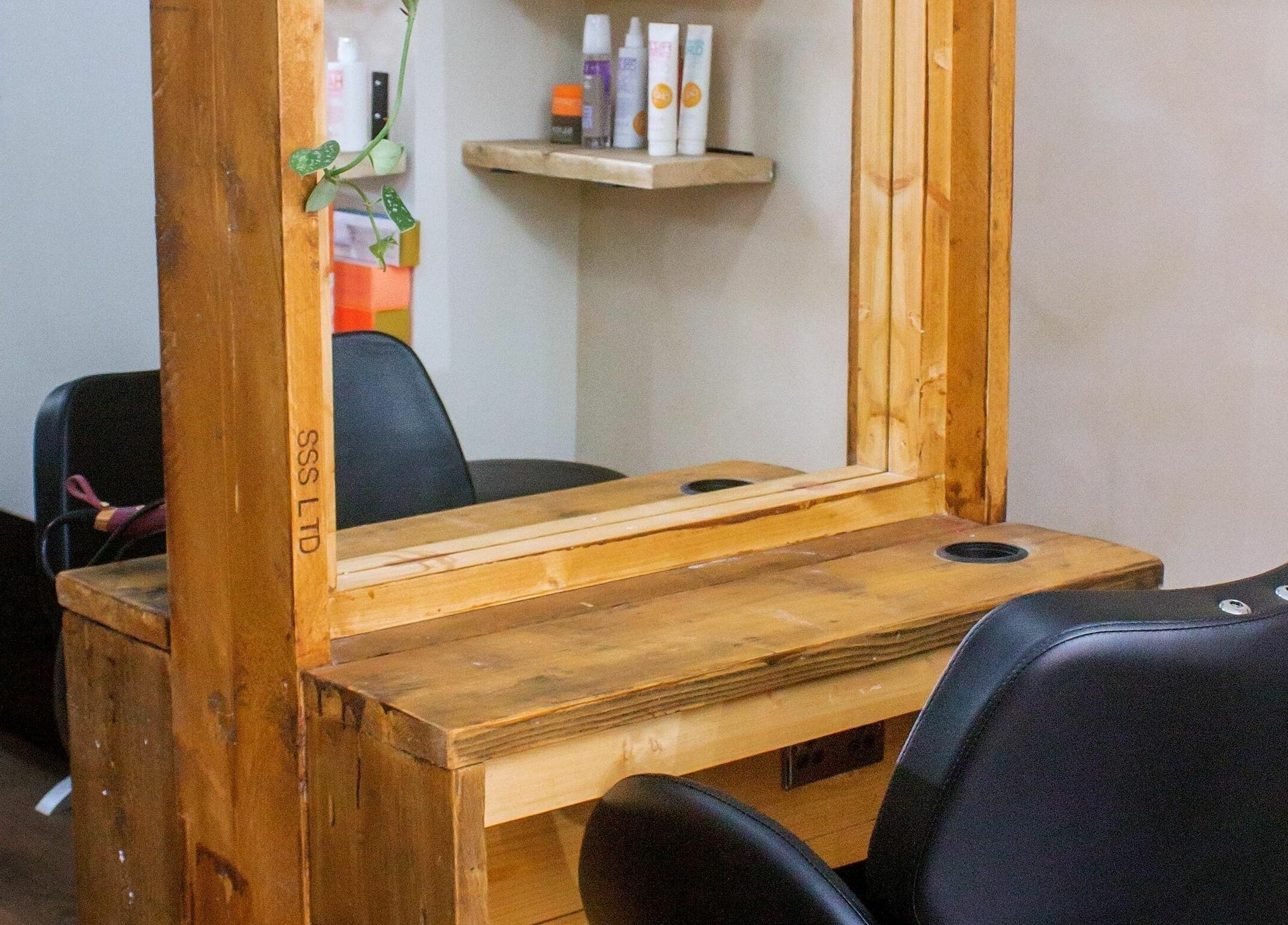 Cozy salon station at The Workhouse Hair, Folkestone, England, GB, with a wooden mirror and black chair.
