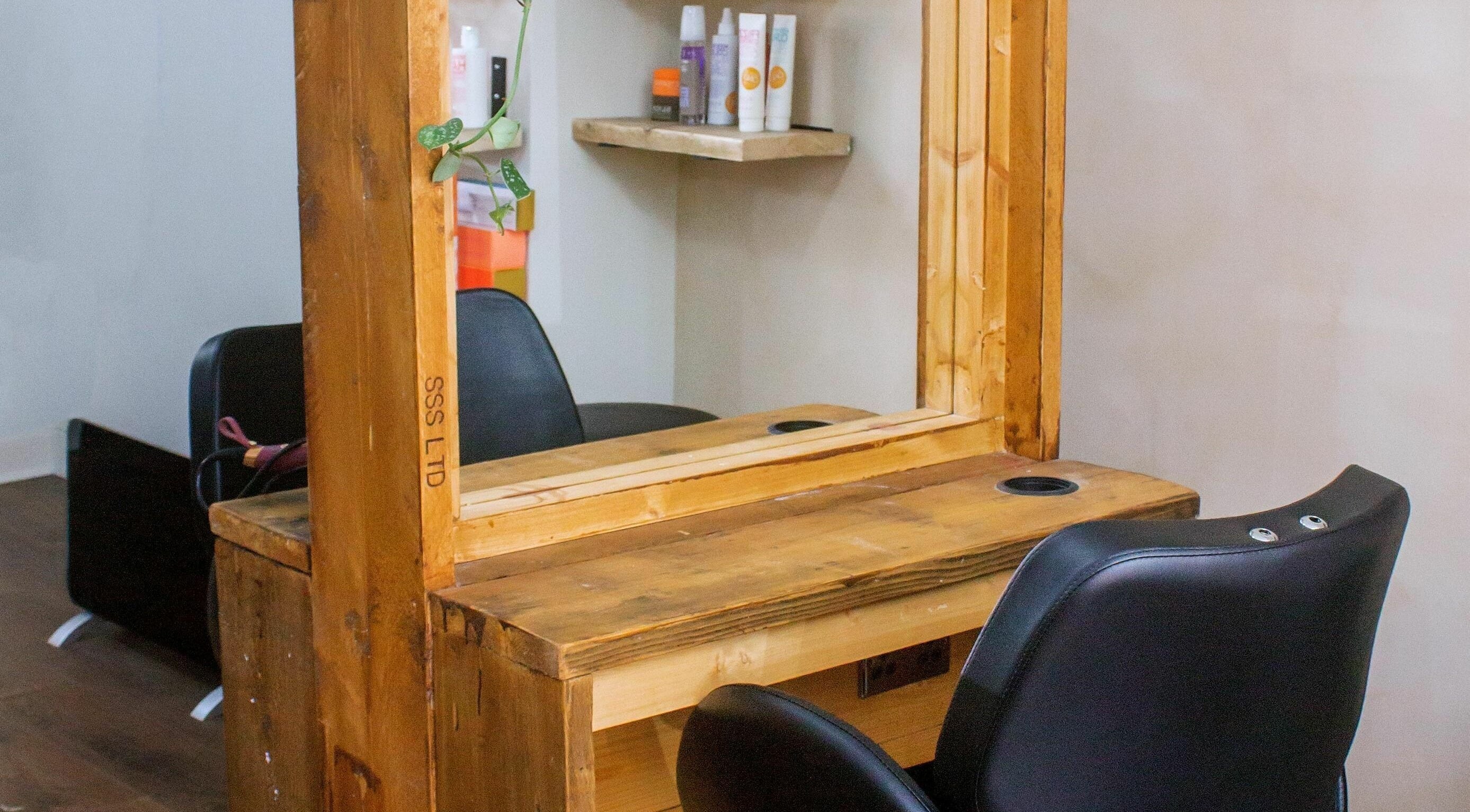 Cozy salon station at The Workhouse Hair, Folkestone, England, GB, with a wooden mirror and black chair.