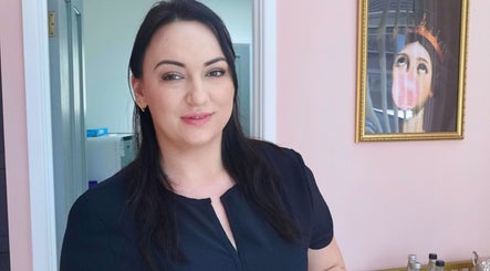 Staff member at New Age Aesthetics, Doncaster, England, GB, welcoming you with a smile in front of pink walls.