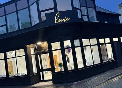 Front view of RENŪ at West Kirby, England, GB, showcasing modern glass windows and elegant interior lighting.