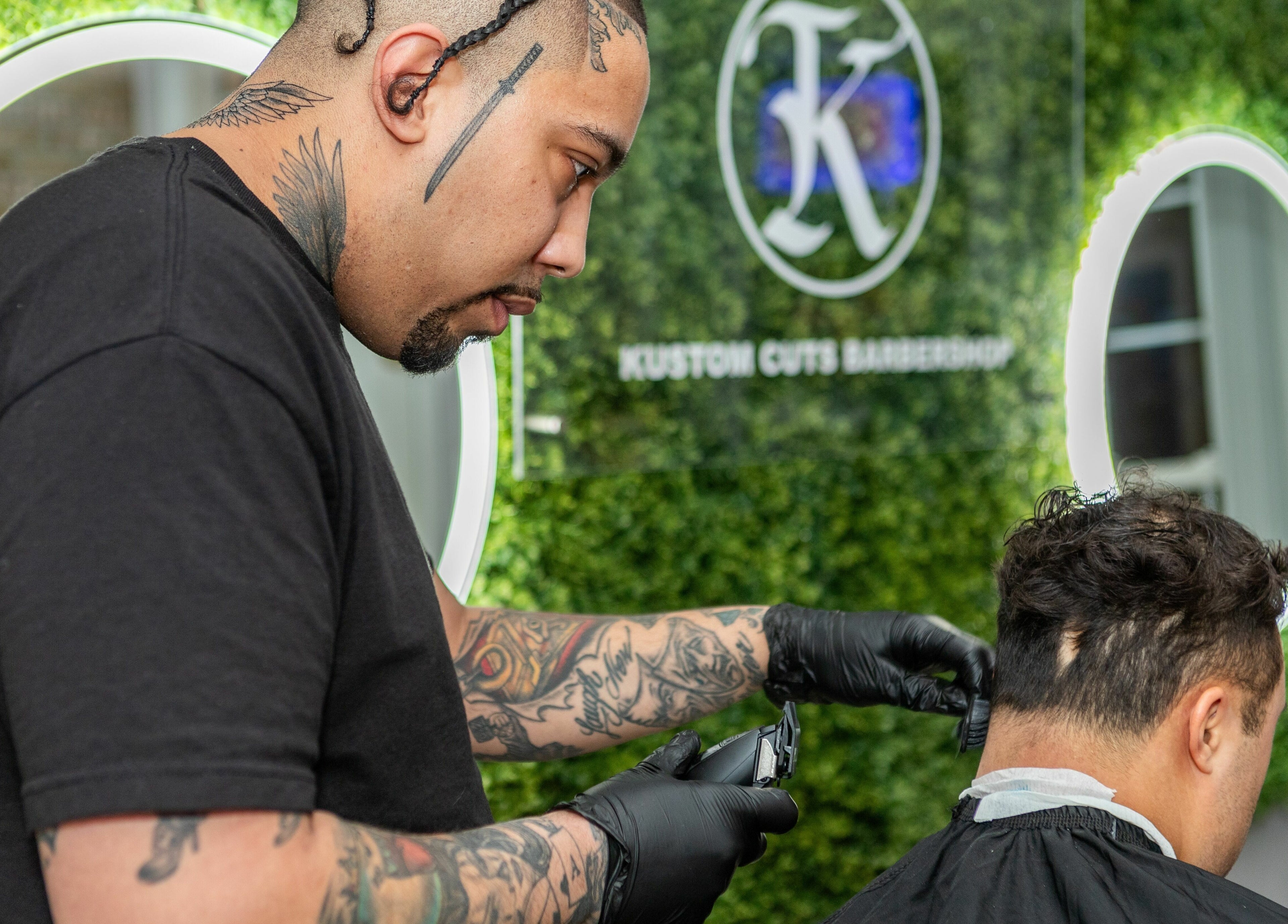 Barber styling a client's hair at KustomCuts in Toronto, Ontario, CA with a greenery backdrop.