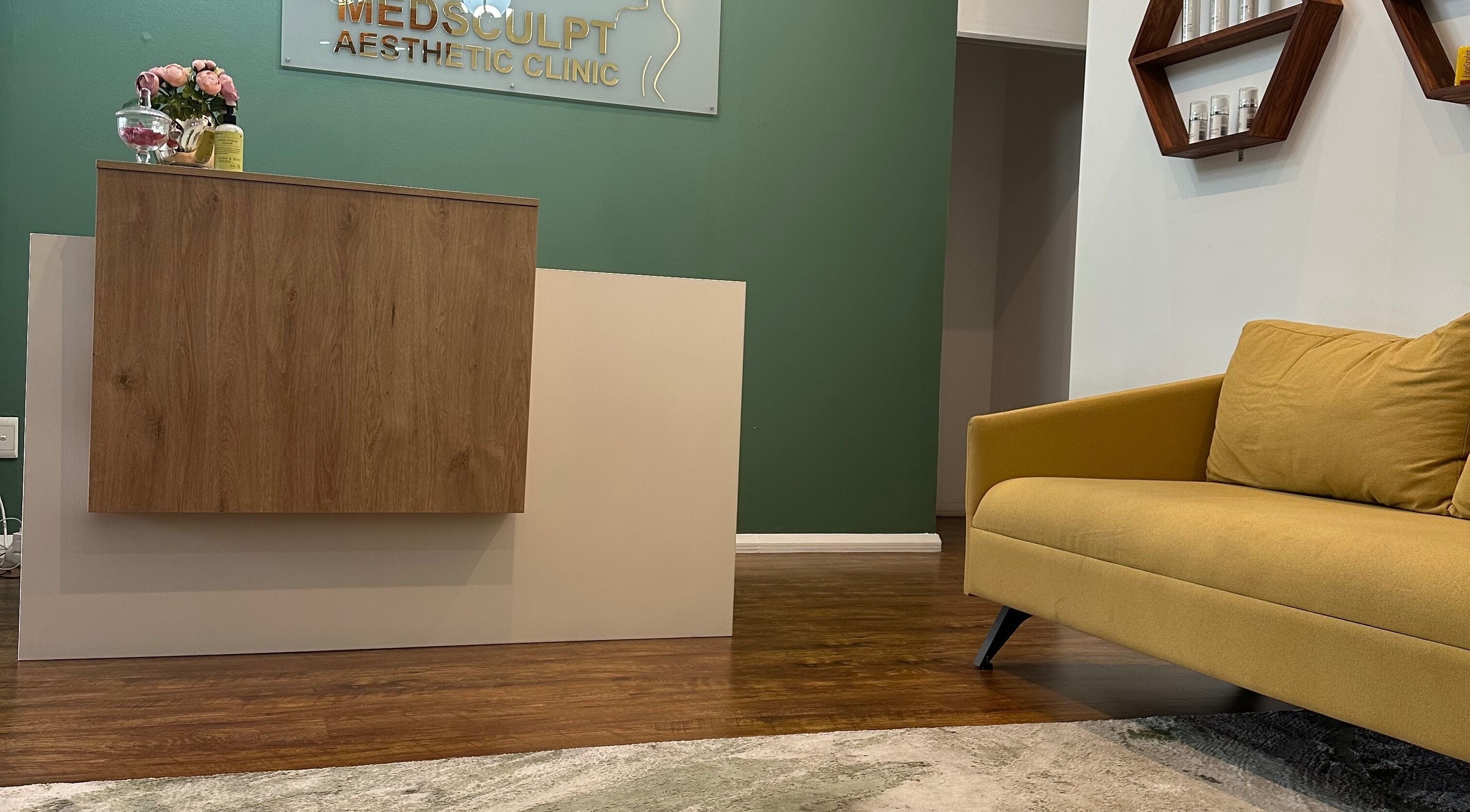 Reception area of Medsculpt Aesthetics Clinic in Pretoria, Gauteng, ZA with a wooden desk and yellow sofa.