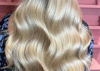 Long, golden wavy hair styled at JessicaLibbyHair in Hinckley, England, GB against a pink backdrop.