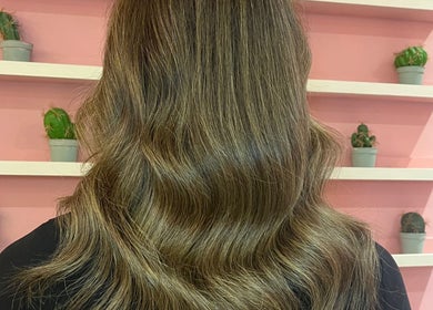 Elegant wavy hairstyle at JessicaLibbyHair in Hinckley, England, GB, with a pink backdrop and potted plants.