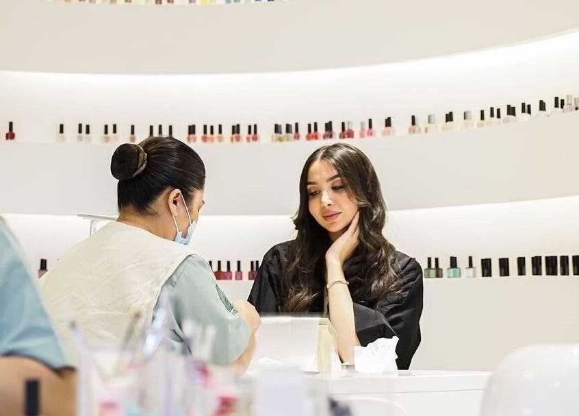 Customer receives nail care at Philautia Salon, Riyadh, Riyadh Province, SA, surrounded by nail polish colors.