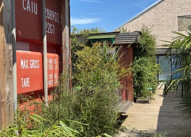Entrance of Massage Margate in Margate, GB with lush greenery and red shipping container wall.