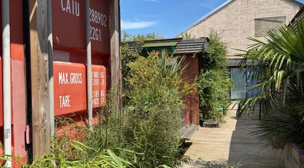 Entrance of Massage Margate in Margate, GB with lush greenery and red shipping container wall.