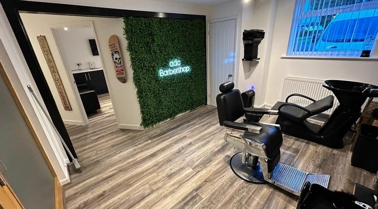 Elegant interior of adc Barbershop in Broadwell, England, featuring stylish chairs and a vibrant green wall.