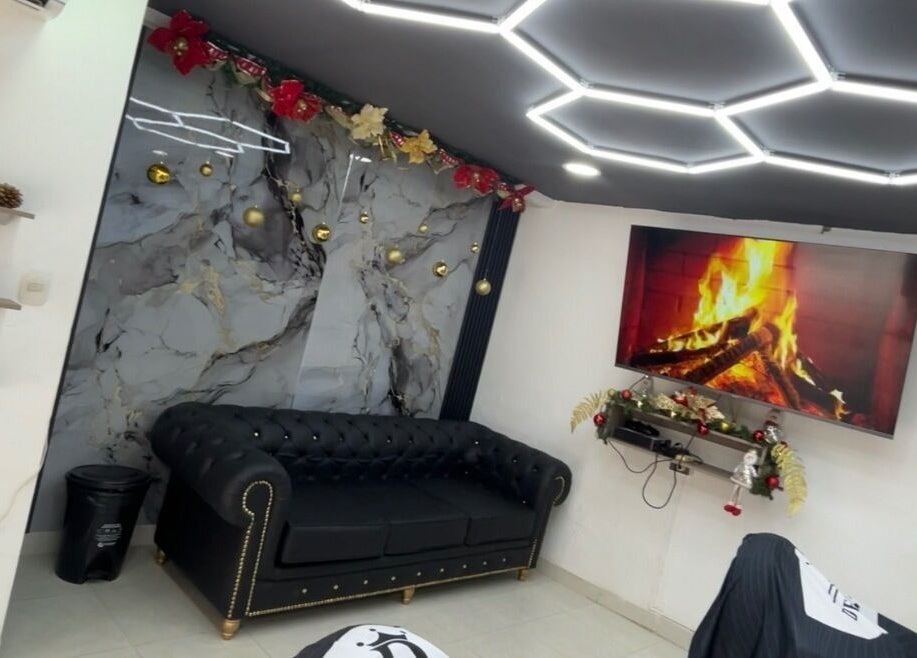 Sala elegante con sofá negro en JR STUDIO BARBER, Granada, Meta, CO, destacando una chimenea y luces modernas.