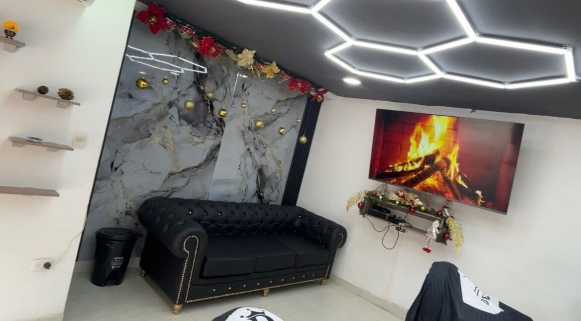 Sala elegante con sofá negro en JR STUDIO BARBER, Granada, Meta, CO, destacando una chimenea y luces modernas.