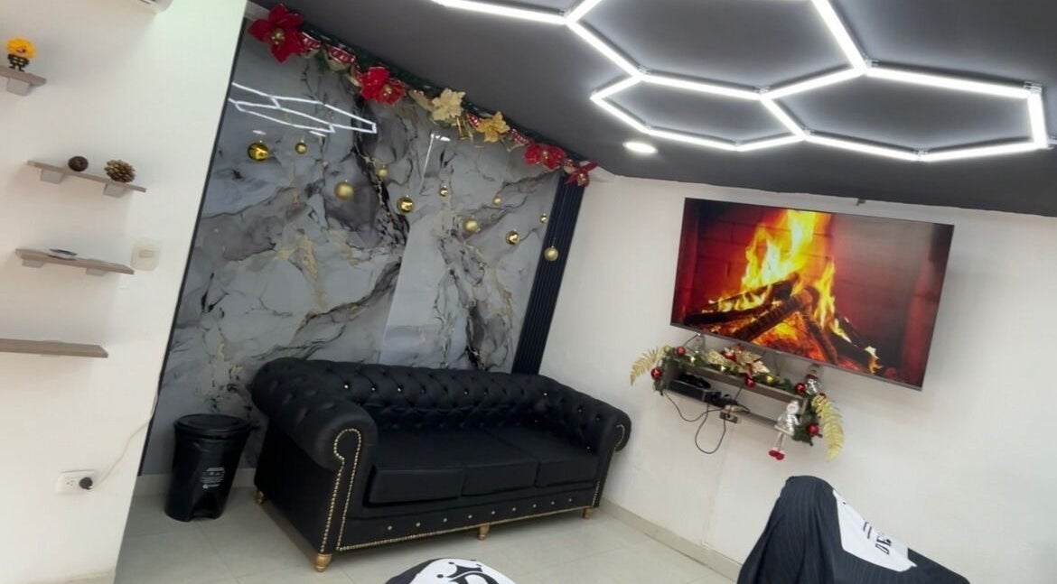 Sala elegante con sofá negro en JR STUDIO BARBER, Granada, Meta, CO, destacando una chimenea y luces modernas.