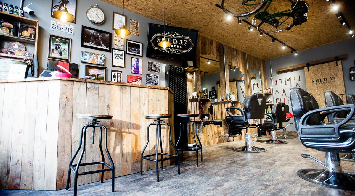 Interior of Shed 37 Barbers in Newport Pagnell, England, GB, featuring rustic decor and modern styling chairs.