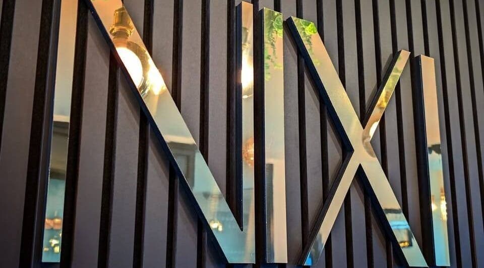 Glossy NIXI Lounge sign on textured wall at Ammanford, Wales, GB, reflecting ambient light.