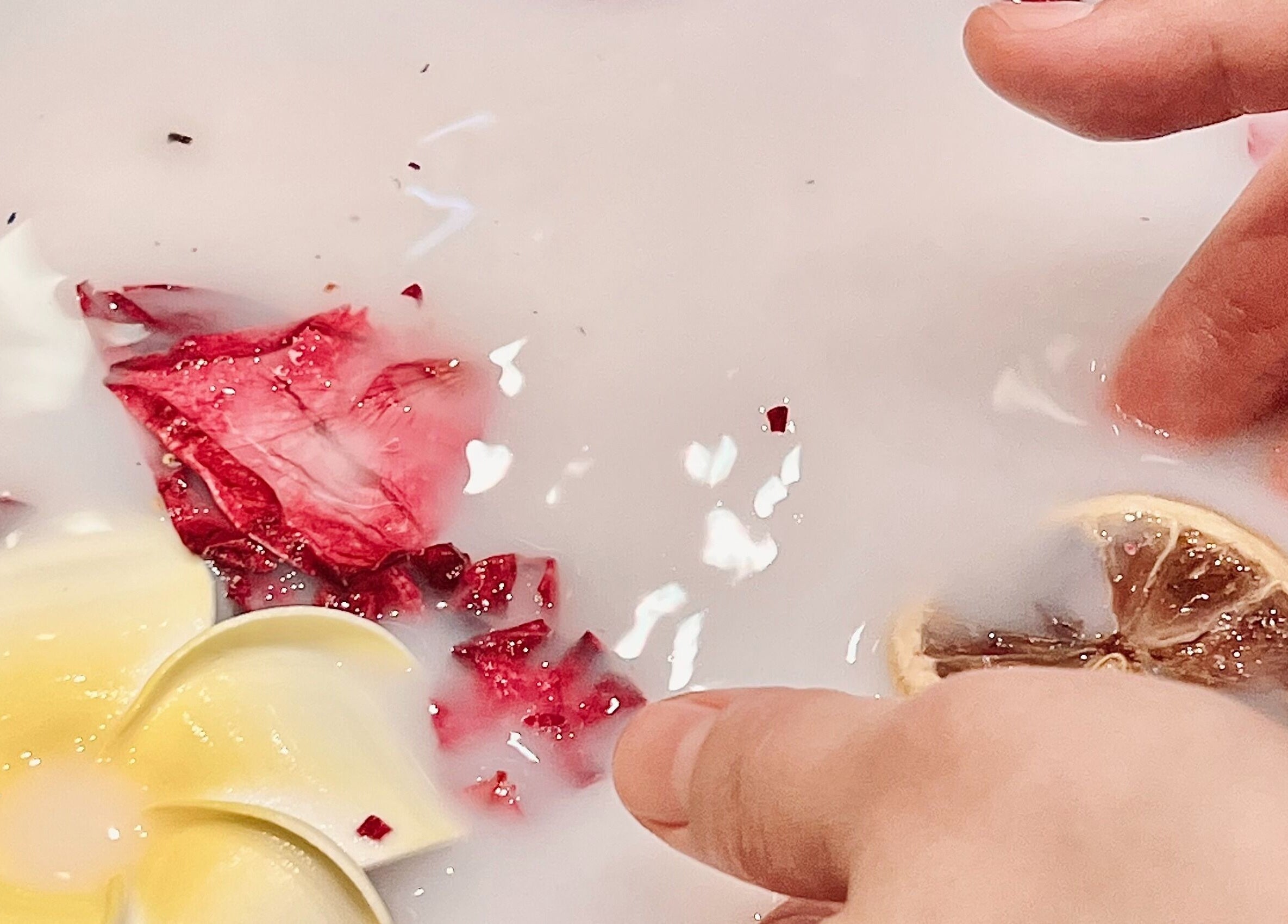 A hand gently dips in a flower and petal-infused milk bath at Healing Arts Essential Spa, Melbourne, Victoria, AU.