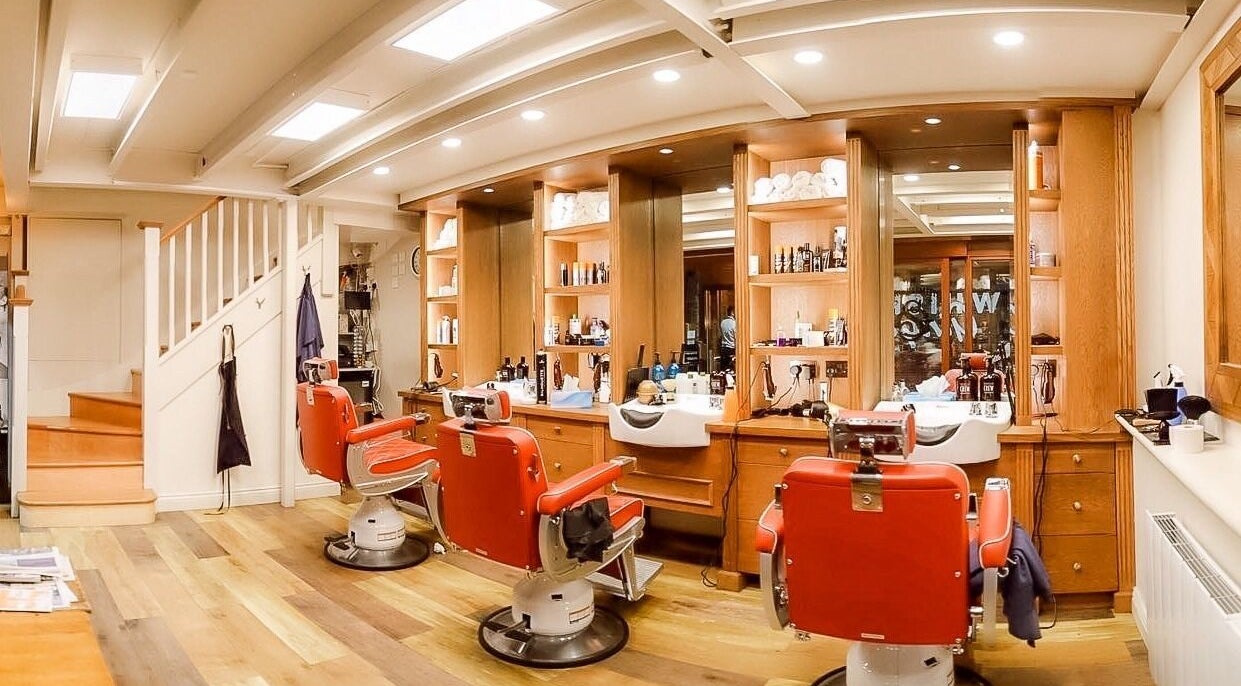 Luxurious barbershop interior at The Groomsmith, London, UK, GB, featuring vintage red chairs and wooden decor.