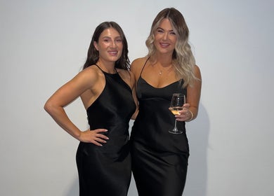 Two women in elegant black dresses at TC Spray Tans event, Nerang, Queensland, AU.