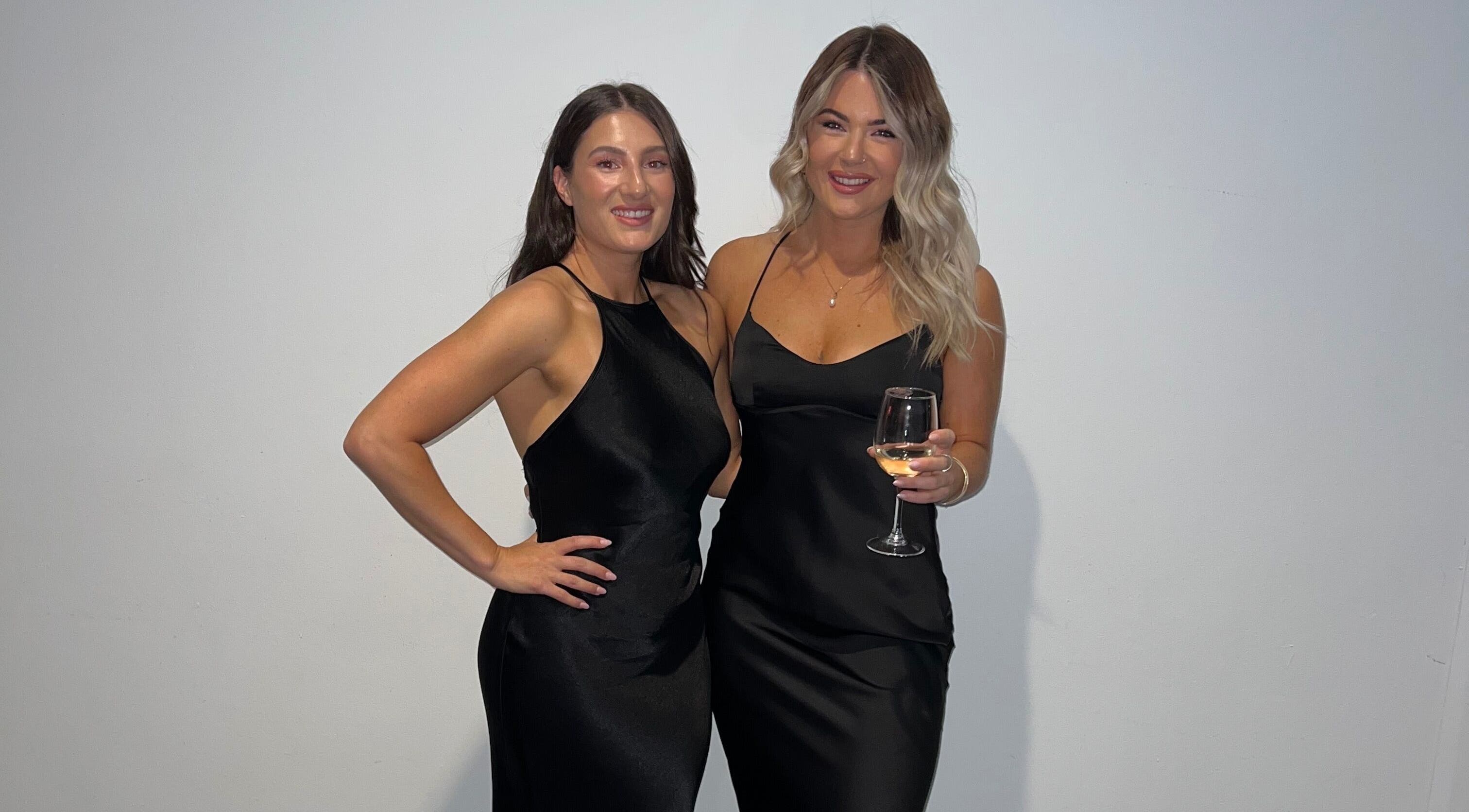 Two elegant women at TC Spray Tans in Nerang, Queensland, AU wearing black dresses, one holding a wine glass.