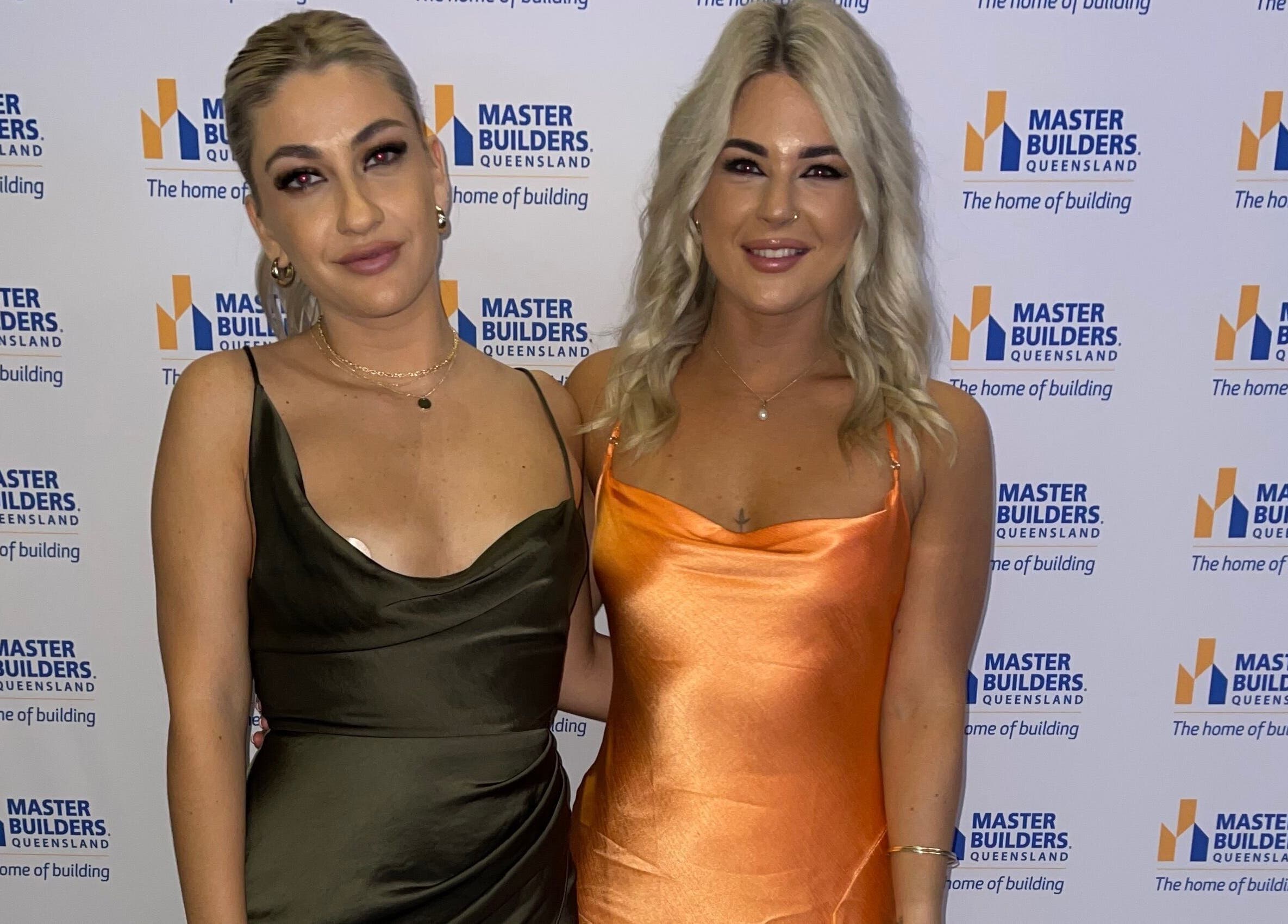 Two women in elegant dresses at a Master Builders event, highlighting TC Spray Tans, Nerang, Queensland, AU.