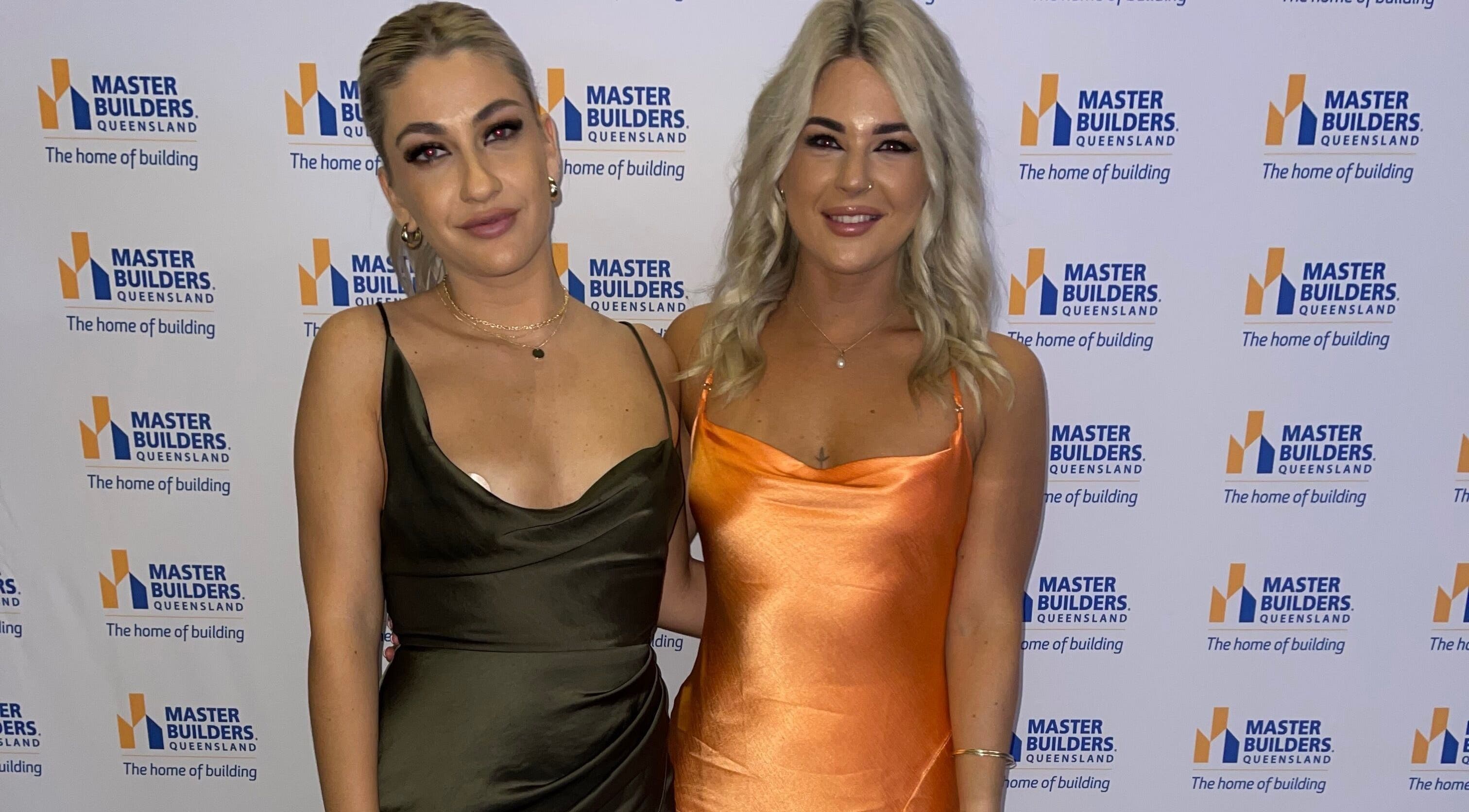 Two women in elegant dresses at a Master Builders event, highlighting TC Spray Tans, Nerang, Queensland, AU.