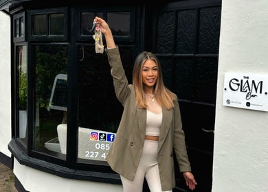 Smiling woman holding keys outside The Glam Bar in Midleton, County Cork, IE, showcasing venue charm.