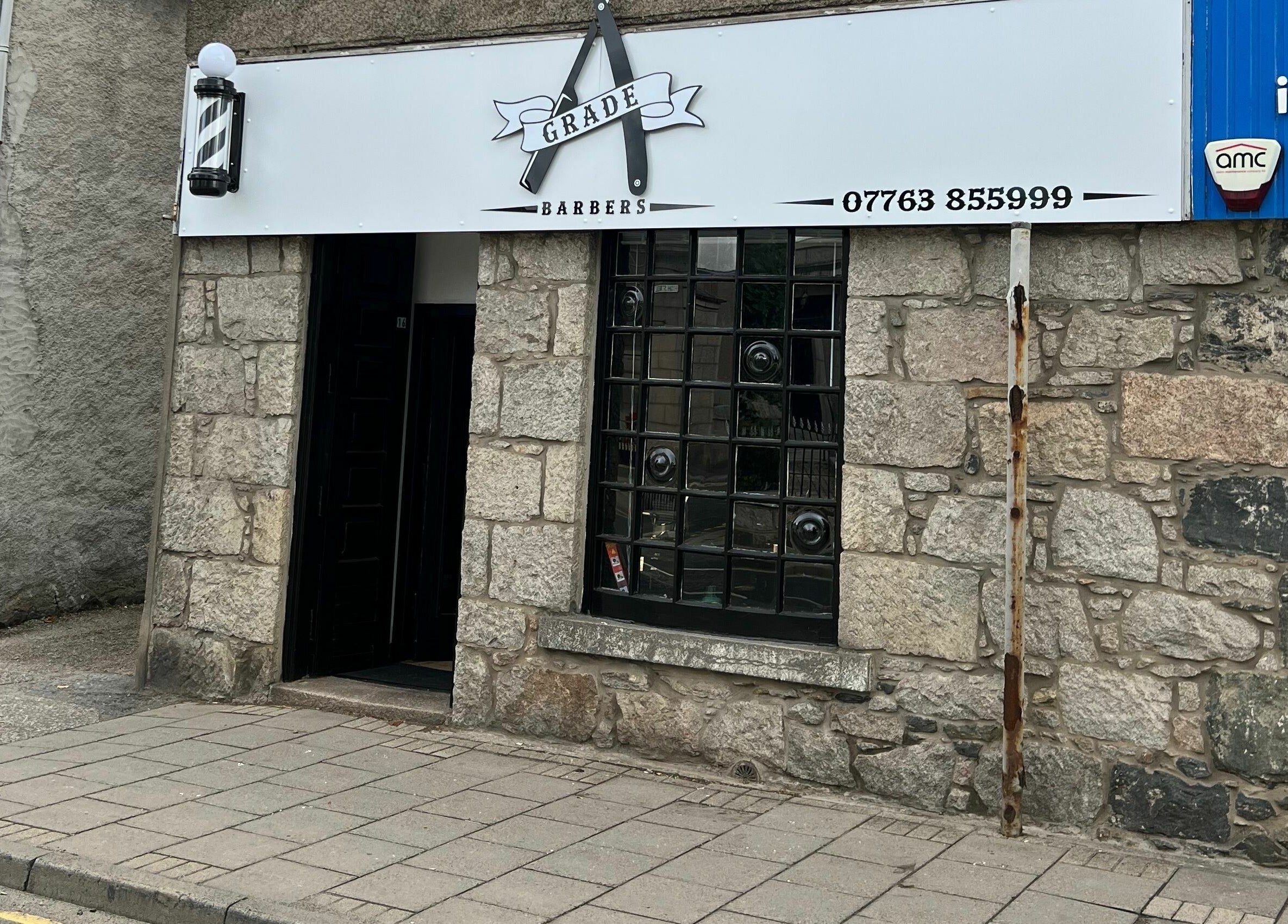 Front view of Grade A Barbers in Inverurie, Scotland, GB with stone facade and barber pole.